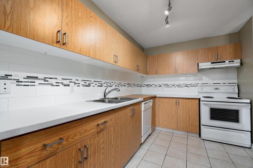 Kitchen featuring wood-finish cabinetry, white countertops, and a subway tile backsplash with decorative mosaic accents - 206 9929 113 Street, Edmonton, AB - Indoor Photo Showing Kitchen With Double Sink