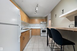 Kitchen featuring light wood cabinetry, white appliances, track lighting, and a breakfast bar with an integrated shelf - 