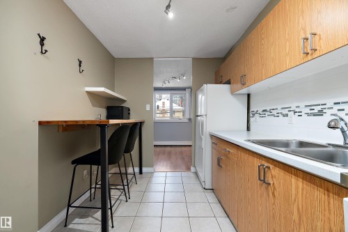 Galley kitchen featuring wood-finish cabinetry, white countertops, and a full-size refrigerator - 206 9929 113 Street, Edmonton, AB - Indoor Photo Showing Kitchen