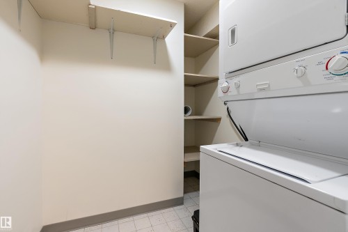 Laundry area featuring a stackable washer and dryer, built-in shelving, and a tiled floor - 206 9929 113 Street, Edmonton, AB - Indoor Photo Showing Laundry Room