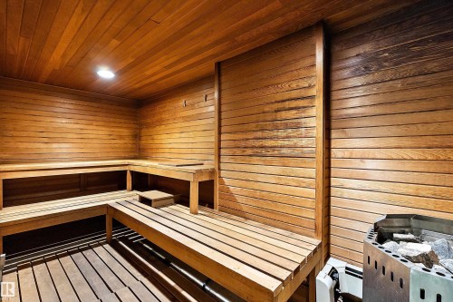 Sauna interior featuring wood-finish walls and ceiling, multi-level wooden benches, and a built-in heating element with stones - 206 9929 113 Street, Edmonton, AB 