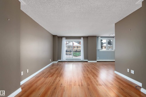 Spacious living area featuring wood-finish flooring, neutral wall paint, white baseboards, and a sliding glass door leading to an exterior balcony - 206 9929 113 Street, Edmonton, AB - Indoor