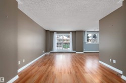 Spacious living area featuring wood-finish flooring, neutral wall paint, white baseboards, and a sliding glass door leading to an exterior balcony - 