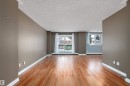 Spacious living area featuring wood-finish flooring, neutral wall paint, white baseboards, and a sliding glass door leading to an exterior balcony - 206 9929 113 Street, Edmonton, AB  - Indoor 