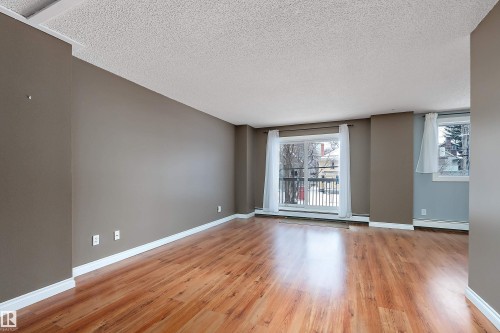 Spacious living area featuring wood-finish flooring, neutral wall tones, and white trim - 206 9929 113 Street, Edmonton, AB - Indoor Photo Showing Other Room