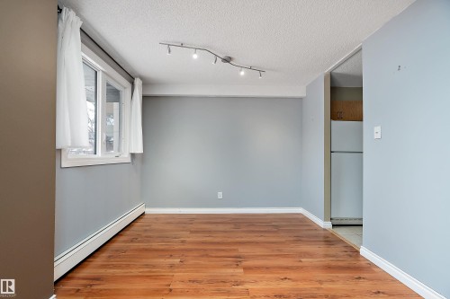 Open area featuring wood-finish flooring, light blue walls, and a window with white trim - 206 9929 113 Street, Edmonton, AB - Indoor Photo Showing Other Room