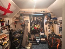 Sloped ceiling storage room featuring built-in shelving, organized tool hanging solutions, and wood-paneling accents - 