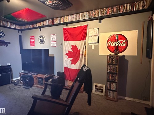 Carpeted room featuring a media console with a television, a built-in shelf above, and a wall-mounted Coca-Cola sign - 10528 100 Avenue, Westlock, AB - Indoor Photo Showing Other Room