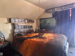 Sloped ceiling room featuring a window with dark drapery, wall-mounted shelving, and a built-in headboard storage unit - 