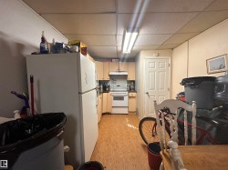 Kitchen area with light wood-finish flooring, light-toned cabinetry, white appliances, and a fluorescent overhead light fixture - 