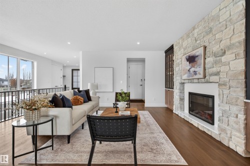 Spacious living area featuring extensive wood-finish flooring, a contemporary linear fireplace with a stone surround, and an open-concept design with a metal railing - 149 Eastgate Way, St. Albert, AB - Indoor Photo Showing Living Room With Fireplace