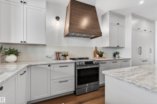 Gourmet kitchen featuring a wood-finish range hood, stainless steel range, light grey cabinetry, light marble-patterned countertops, and wood-finish flooring - 149 Eastgate Way, St. Albert, AB - Indoor Photo Showing Kitchen With Upgraded Kitchen