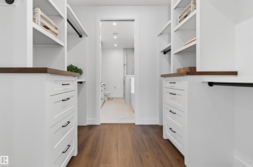 Custom closet system featuring wood-finish flooring, white cabinetry with dark hardware, integrated shelving, and hanging rods - 149 Eastgate Way, St. Albert, AB - Indoor