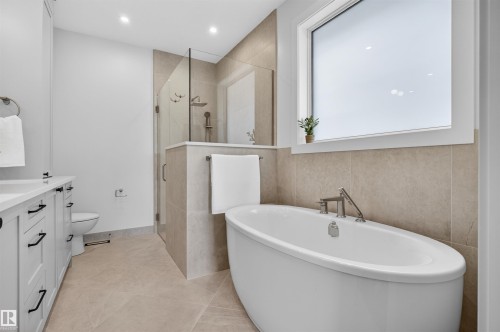 Freestanding soaking tub with chrome fixtures, an adjacent glass-enclosed shower, and a double vanity with white cabinetry and dark hardware - 149 Eastgate Way, St. Albert, AB - Indoor Photo Showing Bathroom