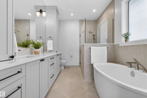 Spacious bathroom featuring a freestanding soaking tub, a large glass-enclosed shower, a double vanity with light gray cabinetry and white countertops, and contemporary black hardware - 149 Eastgate Way, St. Albert, AB - Indoor Photo Showing Bathroom
