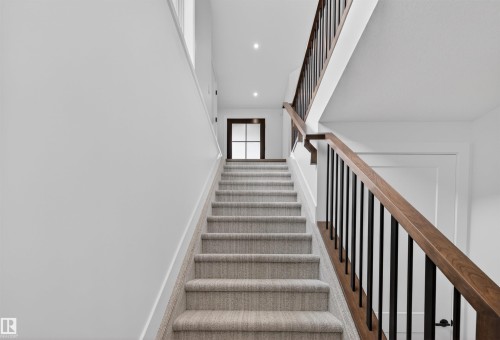 Carpeted staircase featuring a wood handrail with black metal balusters, white trim, and recessed ceiling lighting - 149 Eastgate Way, St. Albert, AB - Indoor Photo Showing Other Room