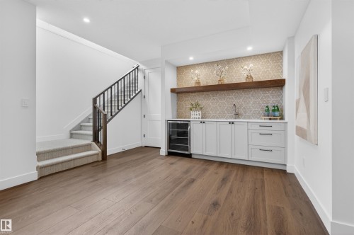 Recreation room featuring wide plank wood-finish flooring, a contemporary wet bar with white cabinetry, light-toned patterned tile backsplash, a dark wood floating shelf, and recessed lighting - 149 Eastgate Way, St. Albert, AB - Indoor Photo Showing Other Room