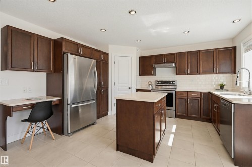 Kitchen featuring dark wood-finish cabinetry, stainless steel appliances, a center island with countertop, a white subway tile backsplash, and light tile flooring - 11539 75 Avenue, Edmonton, AB - Indoor Photo Showing Kitchen With Stainless Steel Kitchen