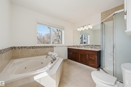Bathroom featuring a corner jetted tub, dual vanity with dark wood cabinetry, a large mirror, and a glass-enclosed shower - 11539 75 Avenue, Edmonton, AB - Indoor Photo Showing Bathroom