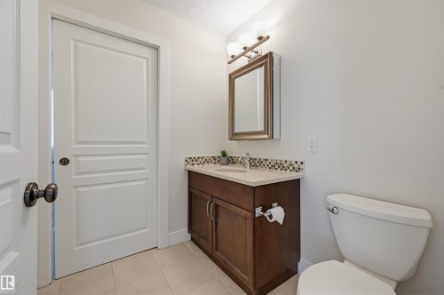Bathroom featuring a dark wood-finish vanity, light countertop, tile backsplash, and a framed medicine cabinet with integrated lighting - 11539 75 Avenue, Edmonton, AB - Indoor Photo Showing Bathroom