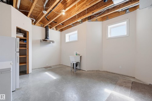 Unfinished basement space featuring exposed ceiling joists, two transom windows, a utility sink, and a stainless steel range hood - 11539 75 Avenue, Edmonton, AB - Indoor Photo Showing Basement