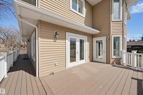 Expansive wood-finish deck with white railing, featuring multiple glass-paneled doors, exterior lighting fixtures, and tan siding - 11539 75 Avenue, Edmonton, AB - Outdoor With Exterior