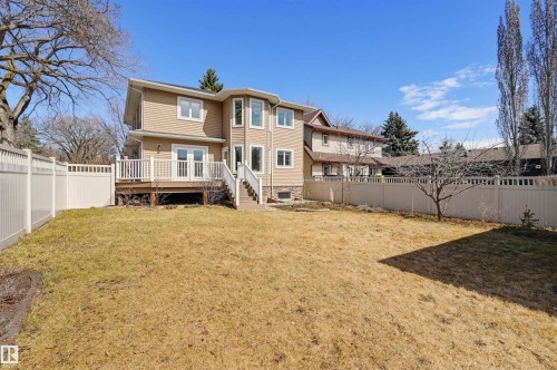 Expansive rear yard featuring a tan vinyl fence, a raised wood deck with white railings, and direct access to the interior via double French doors and a separate stairway - 11539 75 Avenue, Edmonton, AB - Outdoor With Deck Patio Veranda