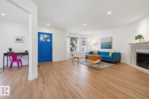 Bright entryway featuring a vibrant paneled door with glass inserts, wood-finish flooring, recessed lighting, a bay window, and a corner fireplace with a stone-finish mantle - 11539 75 Avenue, Edmonton, AB - Indoor Photo Showing Living Room With Fireplace