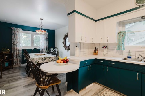 Bright kitchen featuring white upper cabinetry, teal lower cabinetry, white subway tile backsplash, and a double-basin stainless steel sink - 12026 104 Street, Edmonton, AB - Indoor