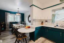 Bright kitchen featuring white upper cabinetry, teal lower cabinetry, white subway tile backsplash, and a double-basin stainless steel sink - 