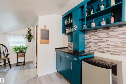Compact wet bar featuring teal cabinetry, open shelving, a black countertop, a stainless steel under-counter refrigerator, and a mosaic tile backsplash - 12026 104 Street, Edmonton, AB - Indoor Photo Showing Other Room