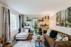 Living area featuring a textured accent wall with floating shelves, wood-finish flooring, and a large window - 