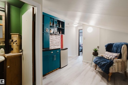 Integrated kitchenette featuring teal cabinetry, dark countertops, a tiled backsplash, and an under-counter refrigerator - 12026 104 Street, Edmonton, AB - Indoor