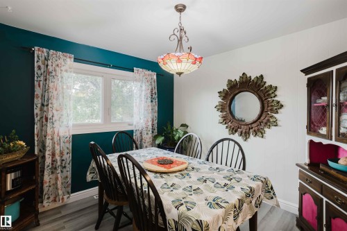 Dining area featuring a central chandelier, wood-finish flooring, white trim, and a double window - 12026 104 Street, Edmonton, AB - Indoor Photo Showing Dining Room