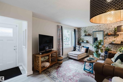 Living area featuring light wood-finish flooring, a textured accent wall, and a large window - 12026 104 Street, Edmonton, AB - Indoor Photo Showing Living Room With Fireplace