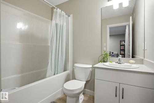 The bathroom features a bathtub with a shower, a toilet, and a vanity with an integrated sink and storage cabinet - 6260 175 Avenue, Edmonton, AB - Indoor Photo Showing Bathroom