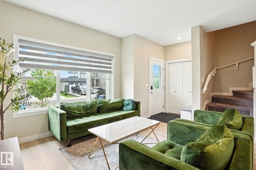 The living area features light-toned walls, light wood flooring, and a large window with horizontal blinds - 6260 175 Avenue, Edmonton, AB - Indoor