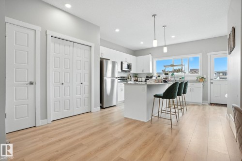 Open concept kitchen featuring an island with seating, pendant lighting, stainless steel appliances, and light-toned flooring - 6260 175 Avenue, Edmonton, AB - Indoor Photo Showing Kitchen With Upgraded Kitchen