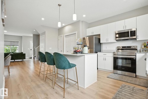 The kitchen features white cabinetry, stainless steel appliances, and a central island with pendant lighting - 6260 175 Avenue, Edmonton, AB - Indoor Photo Showing Kitchen