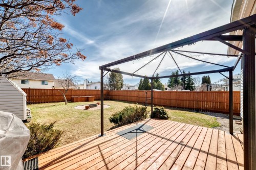 Expansive backyard featuring a wood deck, a metal gazebo structure, a privacy fence, a storage shed, and a circular fire pit area - 9845 184 Street, Edmonton, AB - Outdoor With Deck Patio Veranda