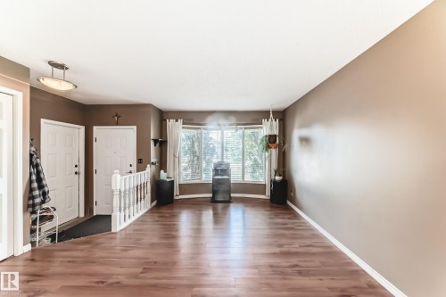 Open-concept living space featuring wood-finish flooring, a prominent bay window, and a white baluster staircase - 9845 184 Street, Edmonton, AB - Indoor Photo Showing Other Room