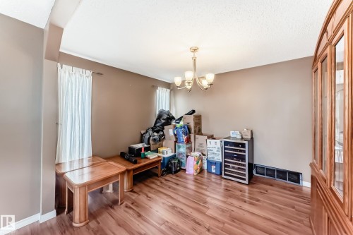 Spacious interior room featuring wood-finish flooring, two windows with white curtains, a multi-bulb chandelier, and a built-in wooden display cabinet with glass panels - 9845 184 Street, Edmonton, AB - Indoor Photo Showing Other Room