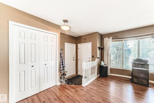 Spacious entryway featuring wood-finish flooring, a bi-fold closet, multiple windows with blinds, and an overhead flush mount light fixture - 9845 184 Street, Edmonton, AB - Indoor Photo Showing Other Room
