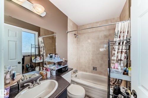 Bathroom featuring a built-in bathtub with shower, light-toned tile surround, and a vanity with an integrated sink - 9845 184 Street, Edmonton, AB - Indoor Photo Showing Bathroom