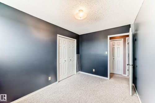 Carpeted room featuring a ceiling-mounted light fixture, two white bi-fold closet doors, and additional white panel doors - 9845 184 Street, Edmonton, AB - Indoor Photo Showing Other Room
