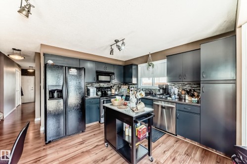 Kitchen featuring dark cabinetry, stainless steel dishwasher, black appliances, wood-finish flooring, and a patterned tile backsplash - 9845 184 Street, Edmonton, AB - Indoor Photo Showing Kitchen