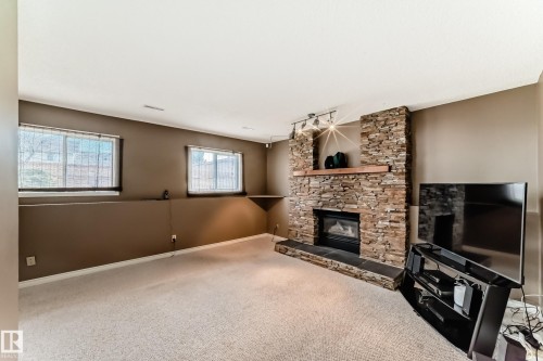 Stone-clad fireplace with a wood mantle, track lighting, and a dark hearth - 9845 184 Street, Edmonton, AB - Indoor Photo Showing Living Room With Fireplace