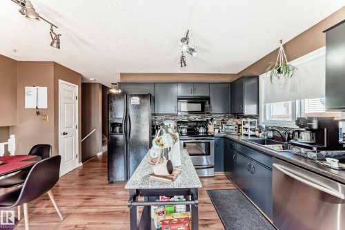 Kitchen featuring dark cabinetry, stainless steel appliances, a tiled backsplash, and wood-finish flooring - 9845 184 Street, Edmonton, AB - Indoor Photo Showing Kitchen With Upgraded Kitchen