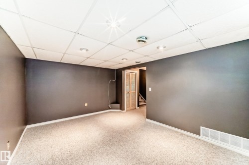 Spacious interior room featuring light-colored carpeting, dark gray walls, and a drop ceiling with recessed lighting - 9845 184 Street, Edmonton, AB - Indoor Photo Showing Other Room