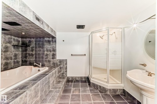 Tiled bathroom featuring a built-in soaking tub, a stand-alone shower with frosted glass, a pedestal sink, and a circular wall mirror - 9845 184 Street, Edmonton, AB - Indoor Photo Showing Bathroom
